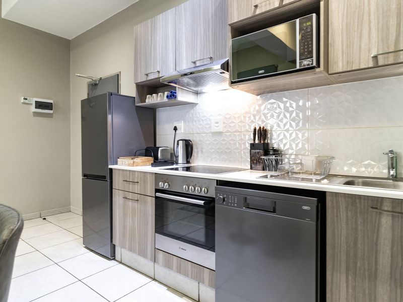 Modern kitchen featuring wood-grain cabinetry, tiled backsplash, integrated appliances including an oven and hob, and durable tiled flooring.