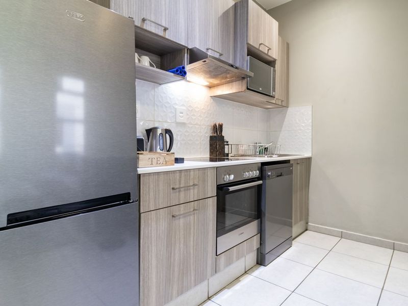 Modern kitchen featuring light wood-grain cabinetry, integrated appliances, a tiled backsplash, and sleek tiled flooring.