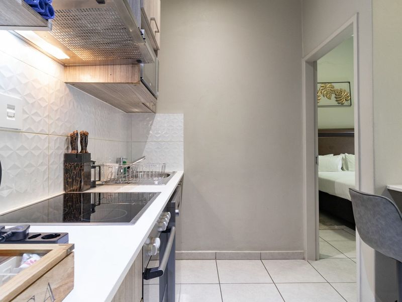 Modern compact kitchen featuring a sleek electric hob, built-in oven, extractor fan, and tiled splashback, with direct access to the adjacent bedroom.