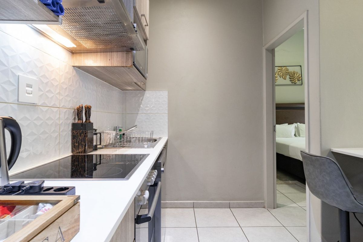 Modern compact kitchen featuring a sleek electric hob, built-in oven, extractor fan, and tiled splashback, with direct access to the adjacent bedroom.