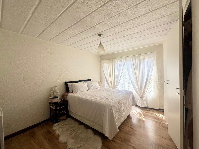 A bright bedroom featuring laminate flooring, a textured ceiling, and a built-in cupboard, with natural light filtering through a glass block window.