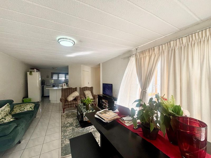 An open-plan living and kitchen area featuring tiled flooring, a breakfast bar, and access to an outdoor space through sliding glass doors.