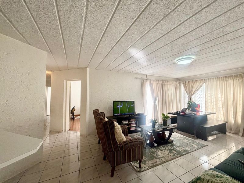 Spacious living area featuring tiled flooring and a textured ceiling, with access to natural light through large sliding glass doors.
