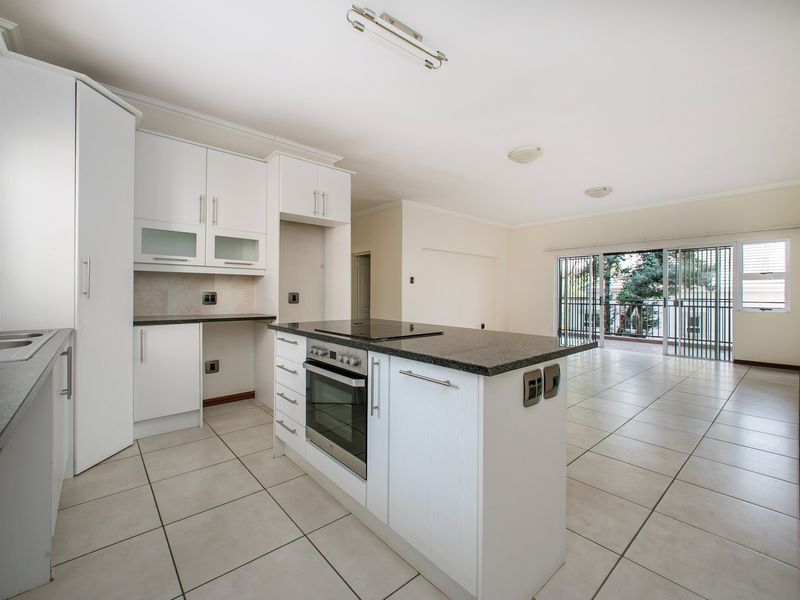 Spacious open-plan kitchen and living area featuring white cabinetry, granite countertops, built-in oven, and direct access to a balcony through sliding glass doors.