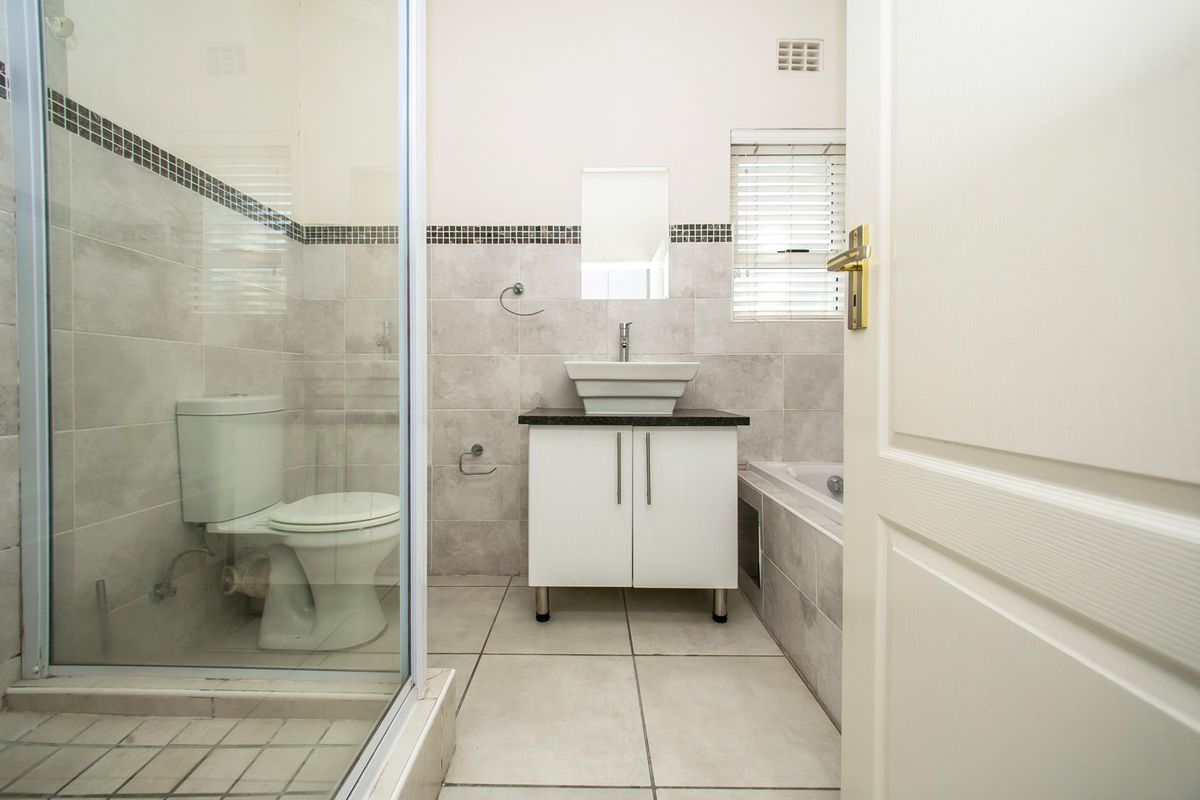 A clean, modern bathroom featuring a glass-enclosed shower, a vessel sink vanity, a bathtub, and neutral floor-to-ceiling tiling.