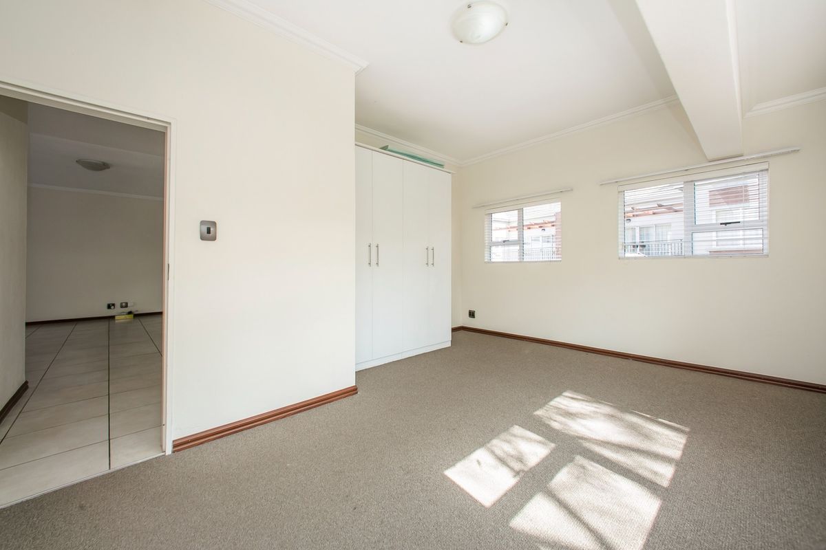 A bright, empty bedroom featuring neutral carpeting, built-in cupboards, and aluminium-framed windows, offering a clean and versatile space.
