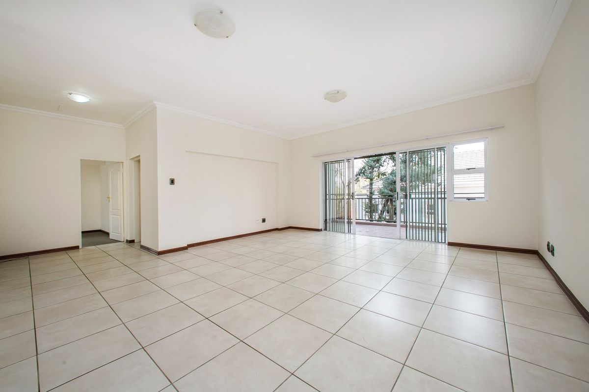 A spacious, empty living area featuring neutral tiled flooring, clean white walls, and large sliding glass doors leading to an outdoor balcony.