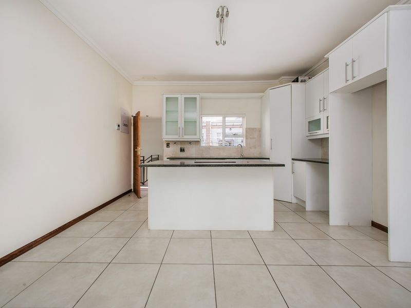 A clean, empty kitchen featuring white cabinetry, granite countertops, a central island, and neutral tiled flooring, offering a blank canvas for customization.