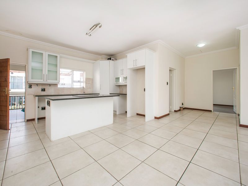 Spacious open-plan kitchen and living area featuring neutral ceramic tile flooring, white built-in cabinetry, stone countertops, and direct access to a balcony.