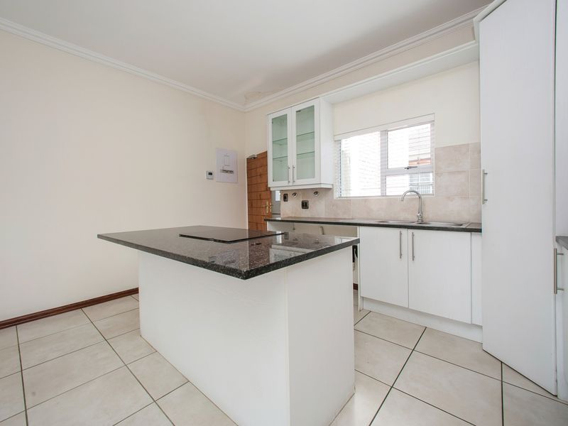 A clean, functional kitchen featuring a central island with a built-in hob, granite countertops, white cabinetry, and tiled flooring.