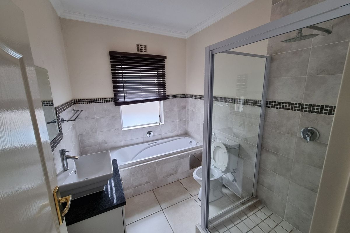 A well-maintained bathroom featuring a glass-enclosed shower, a built-in bathtub, a vessel sink with a granite vanity, and neutral wall and floor tiling.
