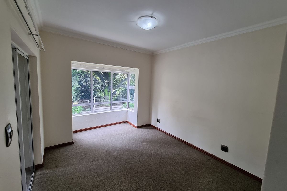 An empty living room featuring carpet flooring, a large bay window providing natural light, and a sliding glass door leading to an outdoor area.