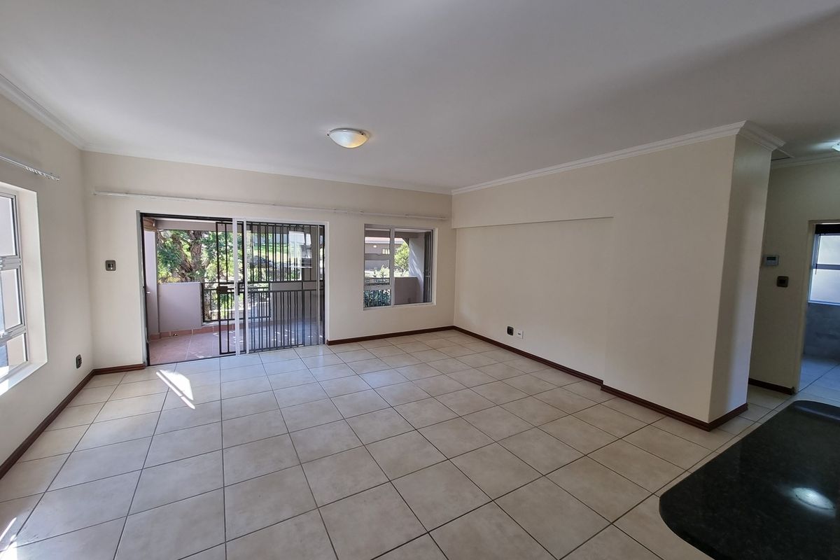 Spacious open-plan living area featuring neutral tiled flooring, ample natural light, and direct access to a private balcony through sliding glass doors.