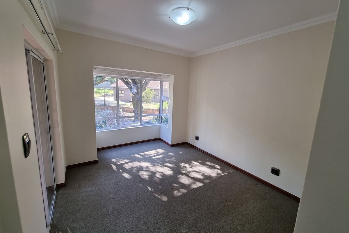 An empty bedroom featuring carpet flooring, a bay window providing natural light, and neutral wall finishes.