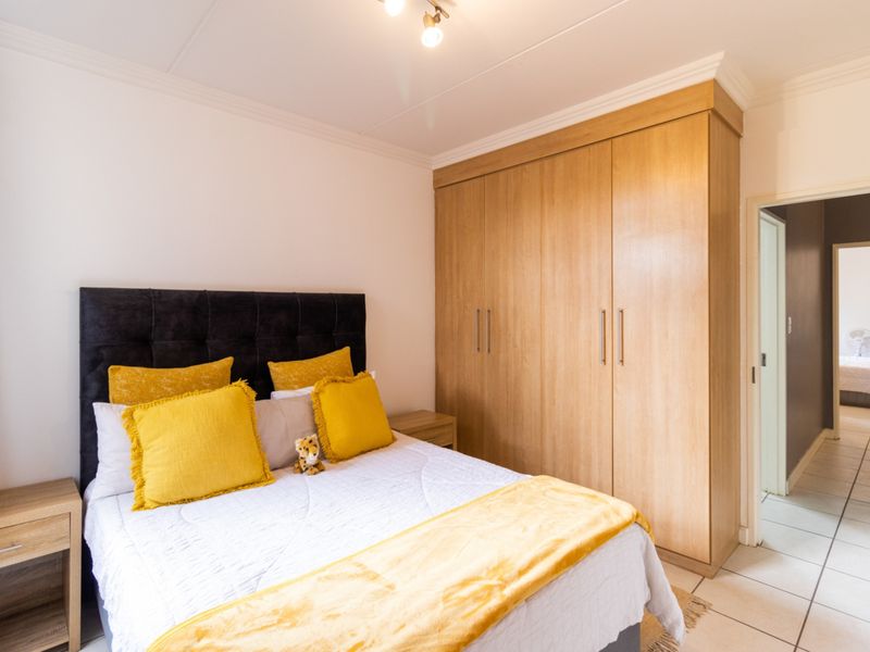 A well-maintained bedroom featuring light wood-finish built-in wardrobes, neutral tiled flooring, and classic ceiling cornicing.