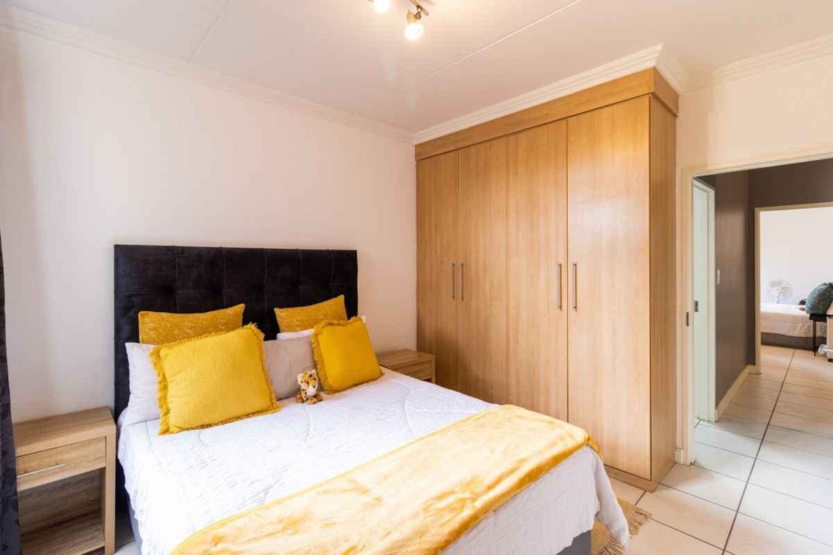A well-maintained bedroom featuring light wood-finish built-in wardrobes, neutral tiled flooring, and classic ceiling cornicing.