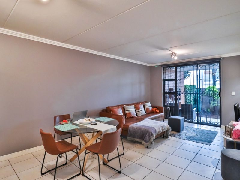Open-plan living and dining area featuring tiled flooring, neutral wall tones, and a sliding glass door with security gate leading to the patio.