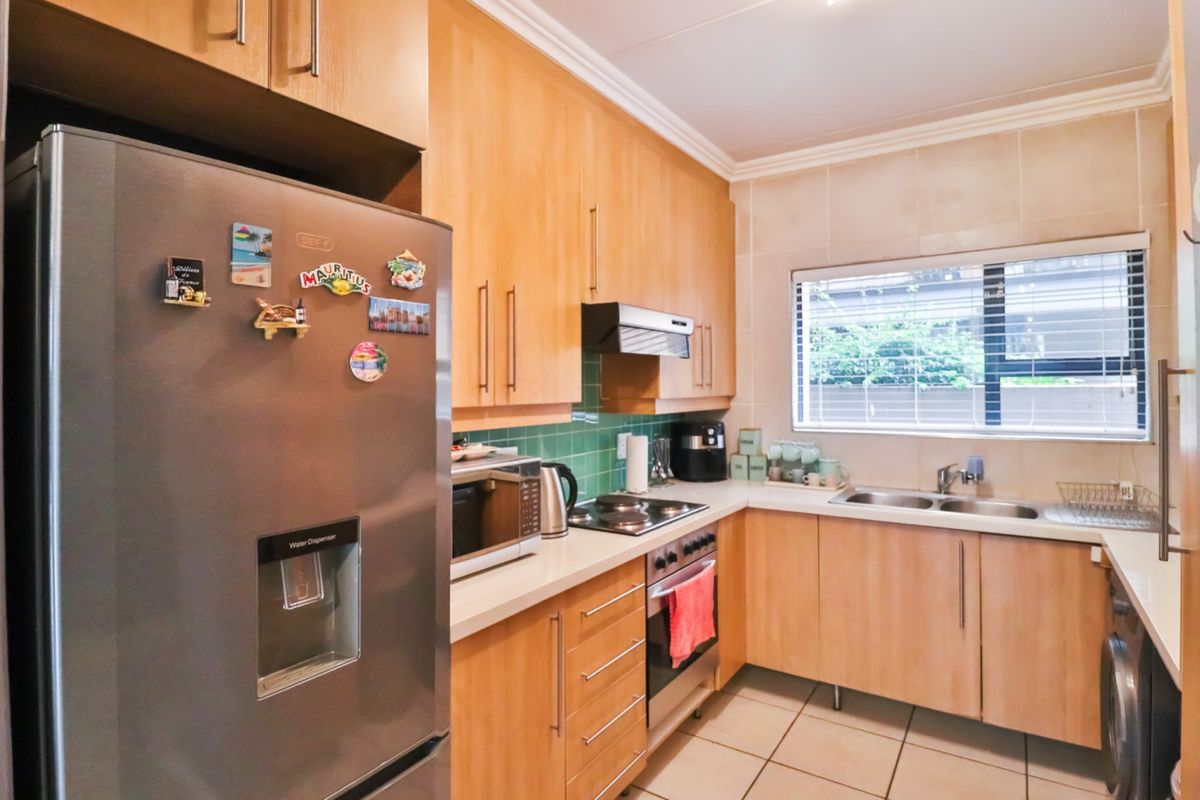 A functional kitchen featuring light wood cabinetry, tiled backsplash, integrated oven and hob, and a stainless steel sink with a window view.