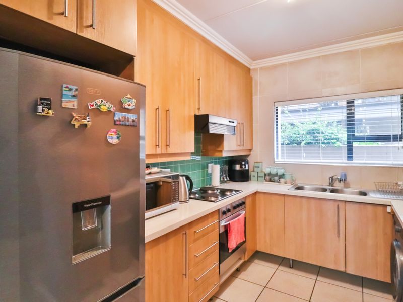A functional kitchen featuring light wood cabinetry, tiled backsplash, integrated oven and hob, and a stainless steel sink with a window view.