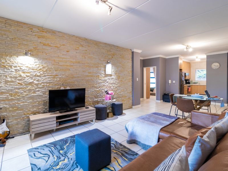 Spacious open-plan living and dining area featuring a textured stone accent wall, neutral tiled flooring, and an integrated kitchen space.