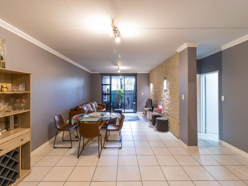 Spacious open-plan living and dining area featuring tiled floors, a textured stone feature wall, and direct access to an outdoor patio through sliding doors.