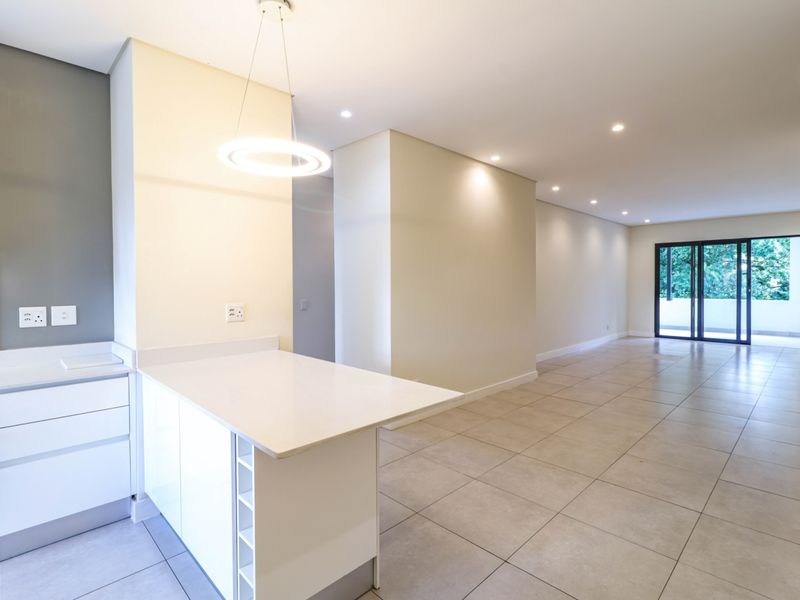 Modern open-plan kitchen and living area featuring sleek white cabinetry, stone countertops, tiled floors, and large sliding doors leading to a balcony.