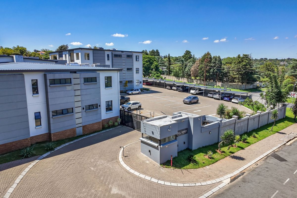 Aerial view of the apartment complex entrance, featuring a security gatehouse, paved driveway, and extensive covered parking facilities.