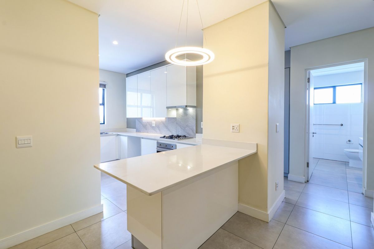 Modern kitchen featuring sleek white cabinetry, stone countertops, a gas hob, and a breakfast bar, with tiled flooring and clean, contemporary finishes.