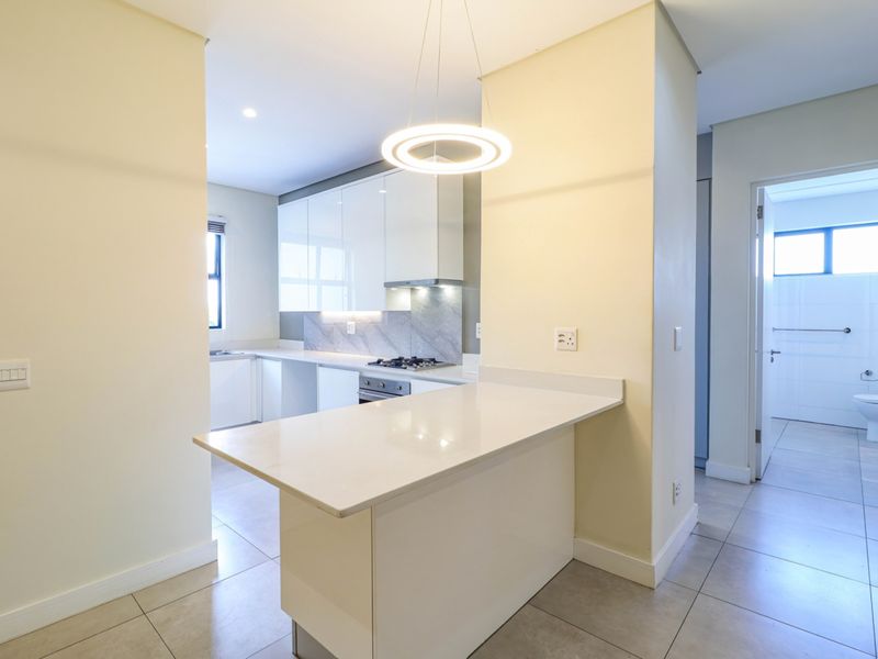 Modern kitchen featuring sleek white cabinetry, stone countertops, a gas hob, and a breakfast bar, with tiled flooring and clean, contemporary finishes.