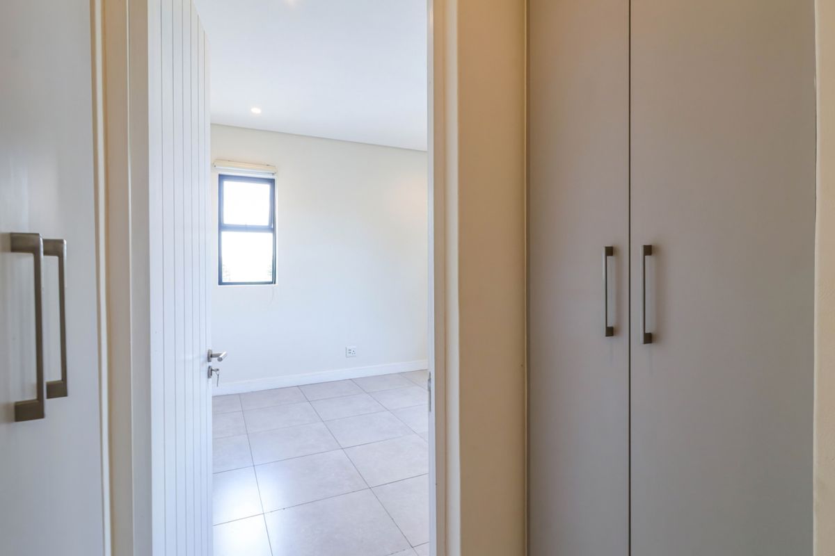 A bright, empty bedroom featuring neutral tiled flooring, built-in cupboards, and a window allowing natural light.