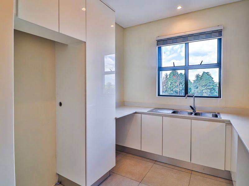 A clean, modern kitchen featuring white built-in cabinetry, a stainless steel double sink, and tiled flooring, offering a bright and functional workspace.