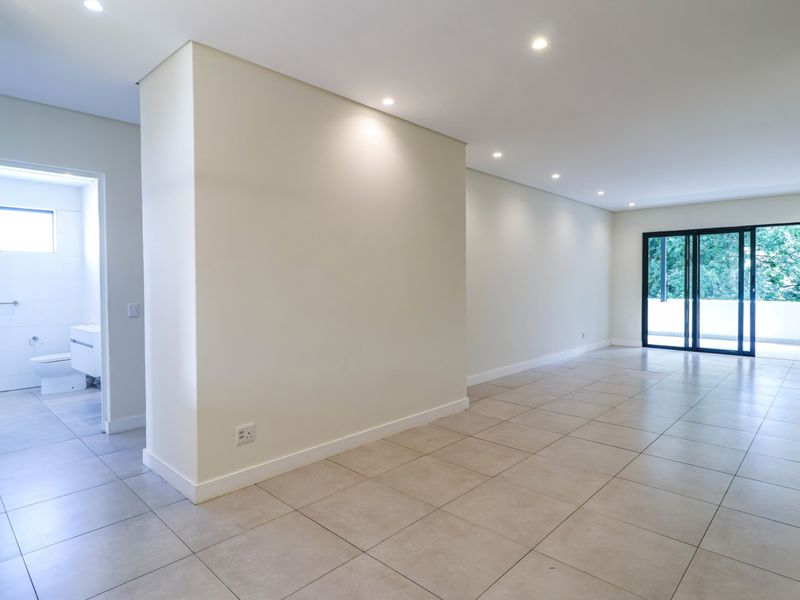 Spacious, modern open-plan living area featuring neutral tiled flooring, recessed downlighting, and large sliding glass doors leading to an outdoor space.