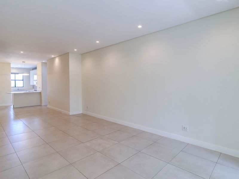 A bright, open-plan living and kitchen area featuring neutral tiled flooring, recessed lighting, and a modern kitchen layout with a central island.
