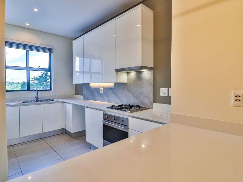 Modern kitchen featuring sleek white cabinetry, stone countertops, integrated gas hob, oven, and extractor fan with neutral tiled flooring.