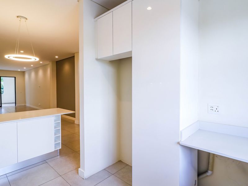Modern kitchen area featuring sleek white cabinetry, a central island, and tiled flooring, offering a clean and minimalist space ready for customization.