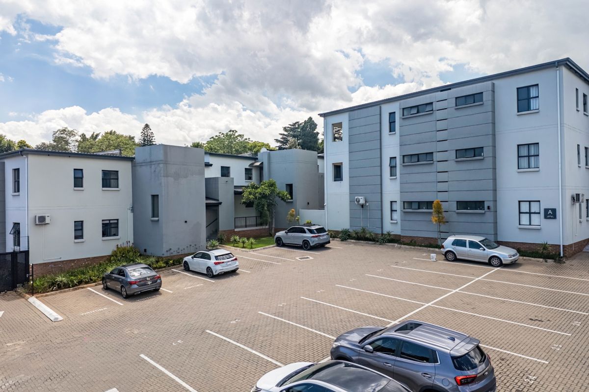 An elevated view of the apartment complex exterior, featuring a paved parking area and multi-story building facades with external air conditioning units.