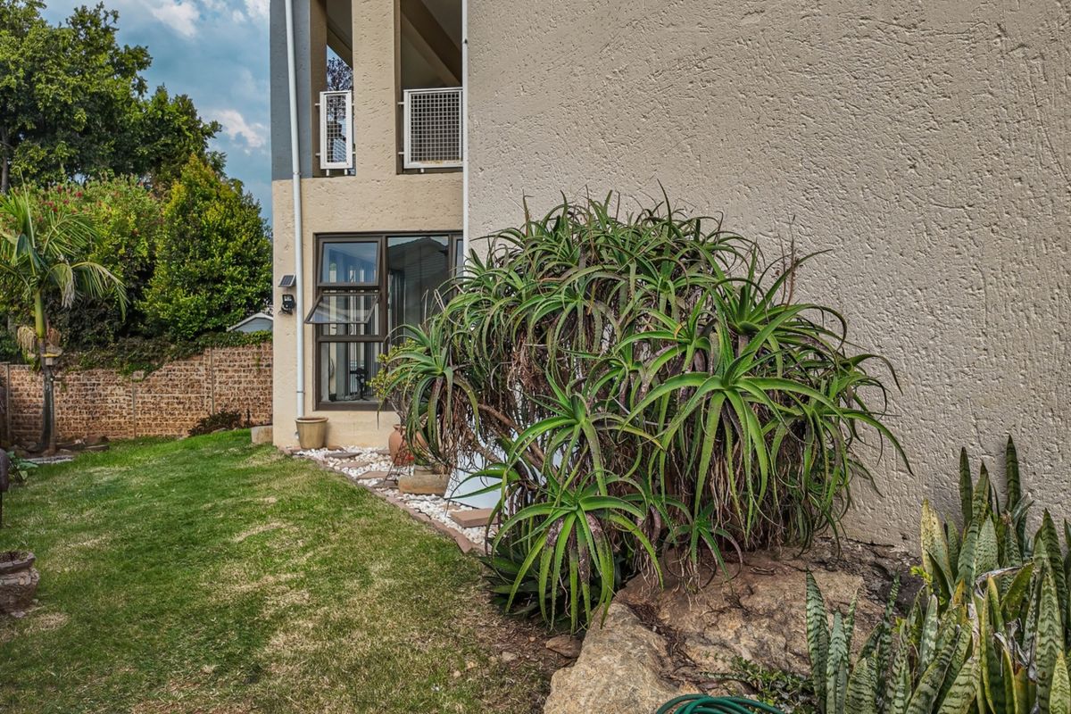 Rear view of the apartment building showing the exterior facade, balcony, and landscaped garden area with established plants.