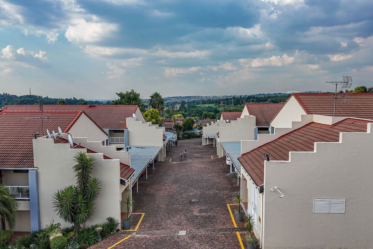 Aerial view of an apartment complex featuring multiple units with tiled roofs, paved driveways, and covered carports.