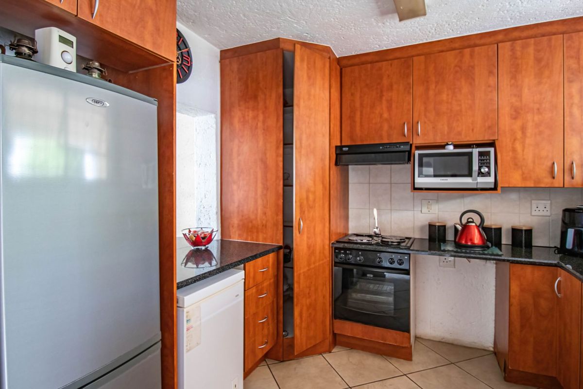 A functional kitchen featuring wood-look laminate cabinetry, granite countertops, a built-in oven with gas hob, and tiled flooring.