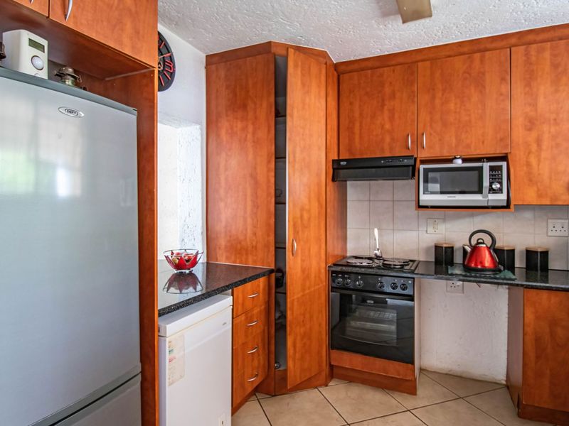 A functional kitchen featuring wood-look laminate cabinetry, granite countertops, a built-in oven with gas hob, and tiled flooring.