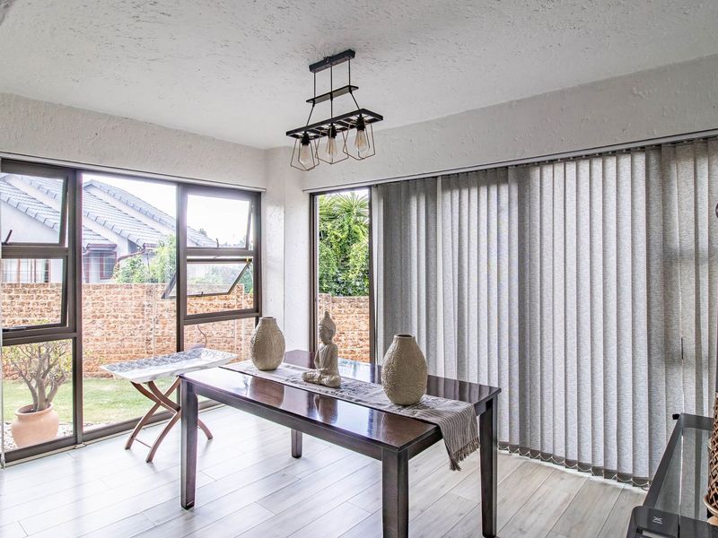A bright dining area featuring laminate flooring, large aluminium-framed windows, and vertical blinds with direct access to the garden.