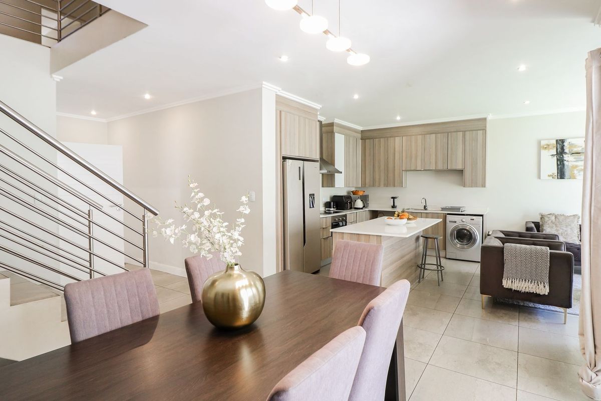 Modern open-plan living area featuring a contemporary kitchen with island, tiled floors, and a sleek staircase with stainless steel railings.