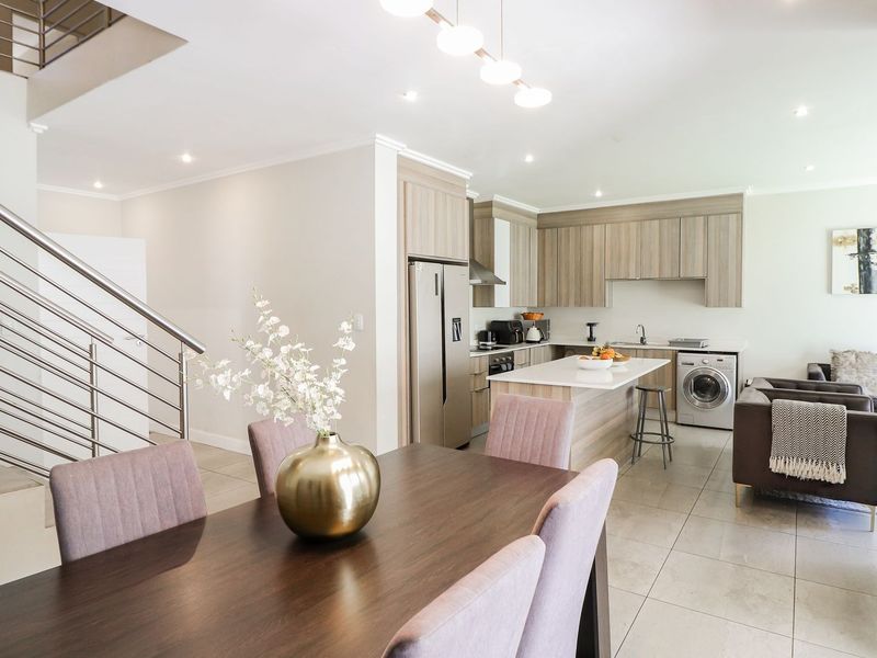 Modern open-plan living area featuring a contemporary kitchen with island, tiled floors, and a sleek staircase with stainless steel railings.