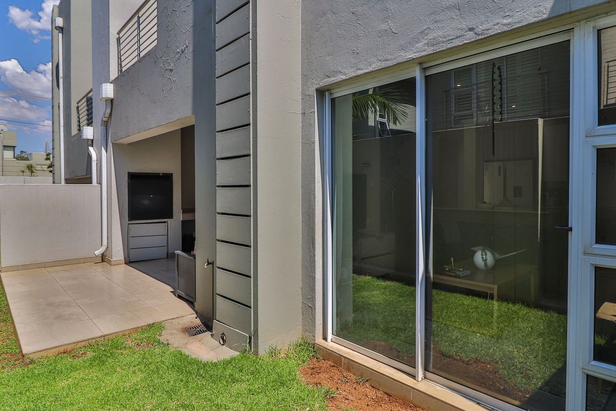 Rear exterior view of the townhouse featuring a tiled patio area with a built-in braai and large sliding glass doors leading to the interior.