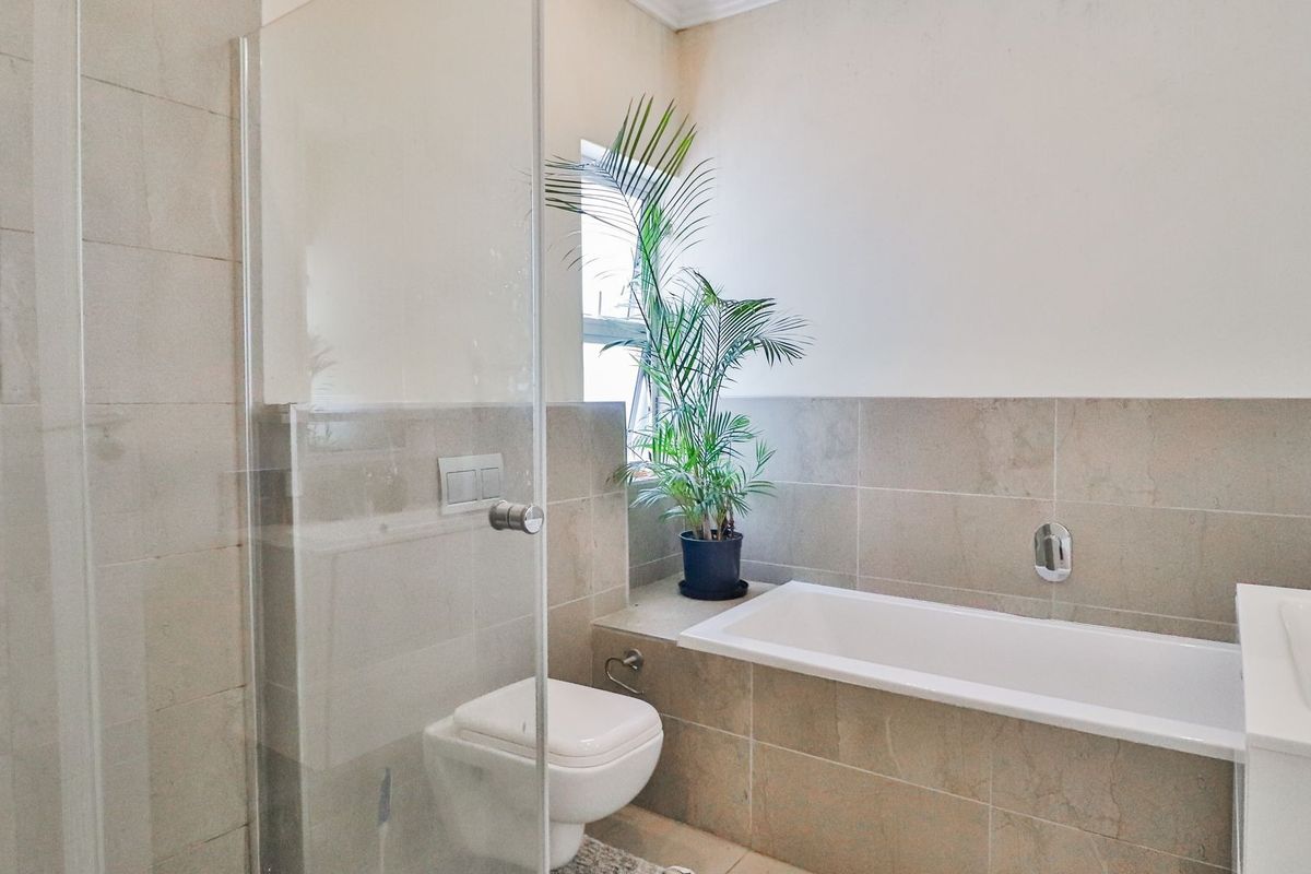 Modern bathroom featuring a glass shower enclosure, wall-mounted toilet, built-in bathtub, and vanity basin with neutral ceramic wall tiling.