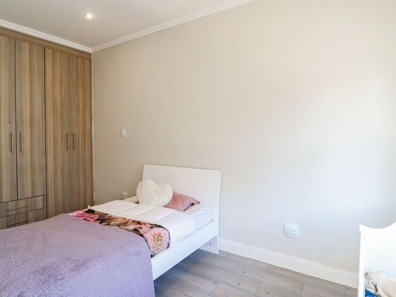 A well-maintained bedroom featuring light-toned laminate flooring, neutral wall finishes, and integrated wooden built-in cupboards providing ample storage space.