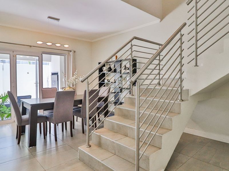 Open-plan living and dining area featuring tiled flooring, a modern staircase with stainless steel railings, and sliding glass doors leading to the patio.