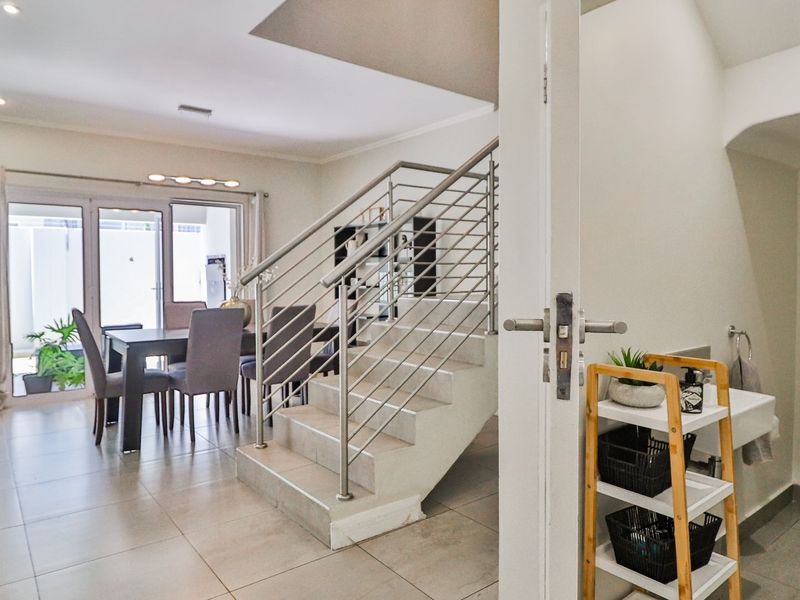 Open-plan living area featuring a modern staircase with stainless steel balustrade, tiled flooring, and direct access to a guest bathroom and patio.