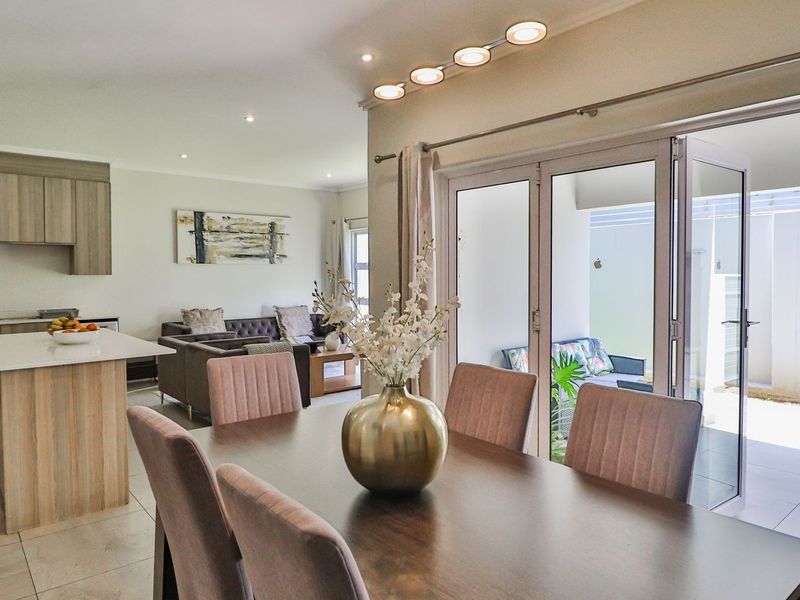 Spacious open-plan living and dining area featuring a modern kitchen with island, tiled floors, and large sliding doors leading to an outdoor patio.