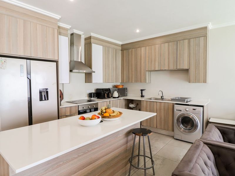 Modern open-plan kitchen featuring light wood-grain cabinetry, stone countertops, a central island, and integrated appliances, seamlessly flowing into the living area.